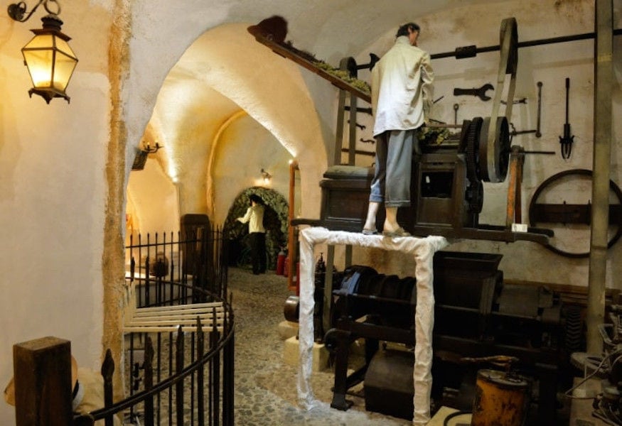exhibit shows a man using grape press machine at 'Koutsoyannopoulos Wine Museum'